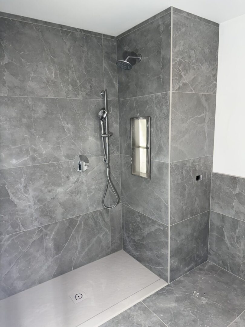 A bathroom with grey tile and a shower.