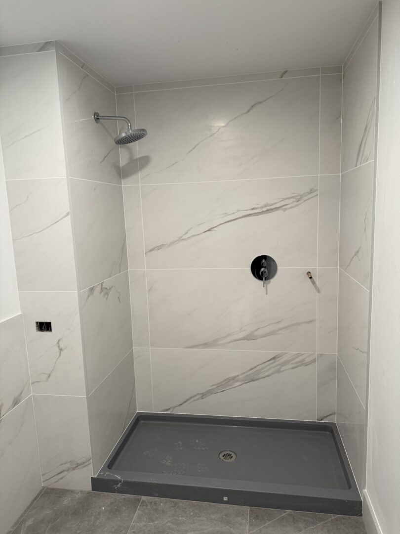 A bathroom with white marble walls and grey floor.
